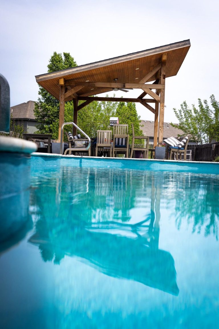Swimming pool with seating area underneath a pergola - Pools By York